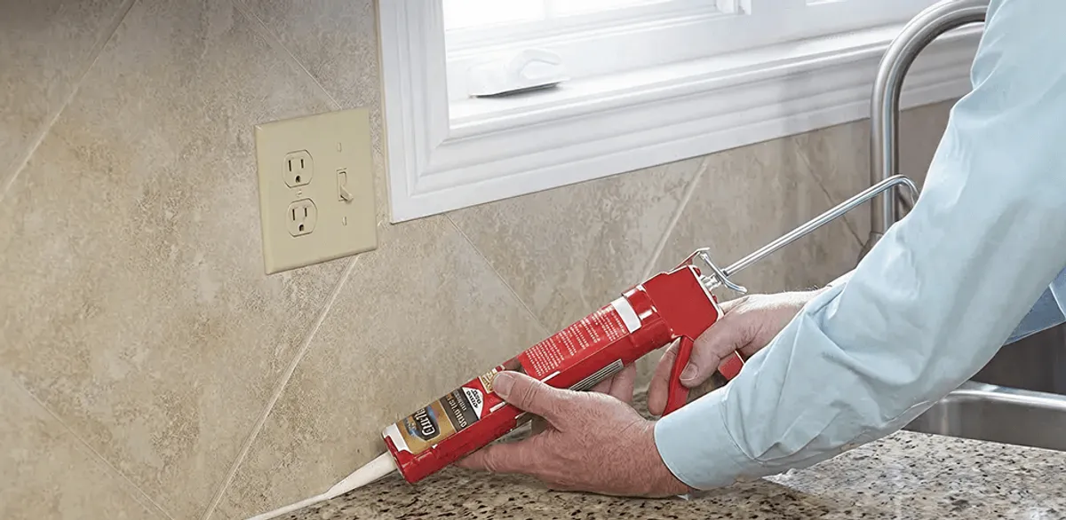 Handyman applying caulk along a kitchen backsplash and countertop seam in Columbus, GA
